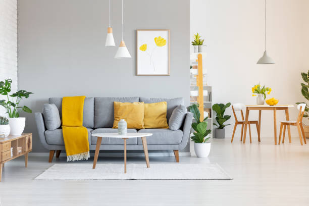 Orange blanket on grey sofa in modern apartment interior with poster and wooden table. Real photo